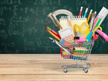 A shopping cart filled with school supplies set against a chalkboard background.